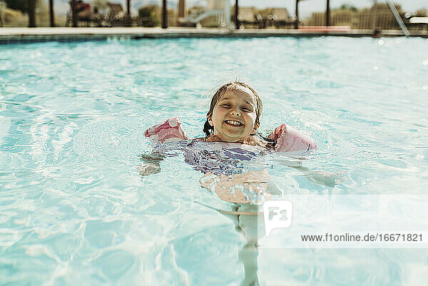 Lifestyle portrait of young girl swimming in hotel pool on vacation