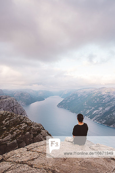 Mann sitzt in einem Felsen am Rande einer Klippe am Preikestolen  Norwegen
