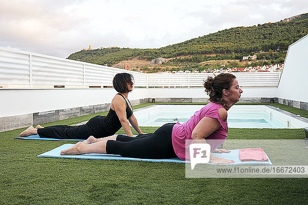 Zwei Frauen üben Yoga auf der Terrasse des Hauses halbe Kobra-Haltung