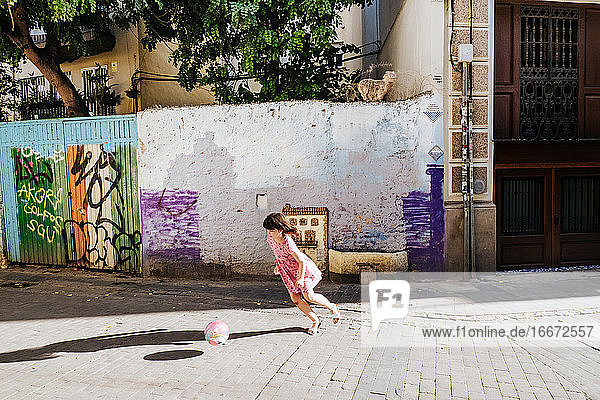 junges Mädchen spielt Fußball in einer bunten Straße