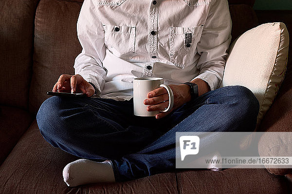 Nahaufnahme eines jungen Mannes  der auf sein Smartphone schaut  während er auf einer Couch sitzt
