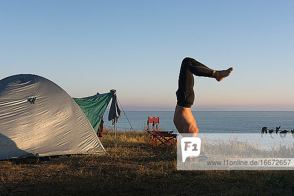 Erwachsener Mann macht Yoga bei Sonnenaufgang  vor dem Zelt am Meer