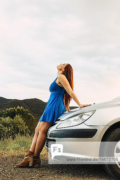 Junge Frau steht an ein Auto gelehnt und schaut allein in der Natur nach oben