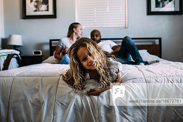 young girl playing on the end of the bed with parents in background