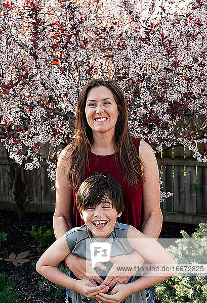 Mutter und junger Sohn umarmen sich vor blühenden Bäumen im Garten.