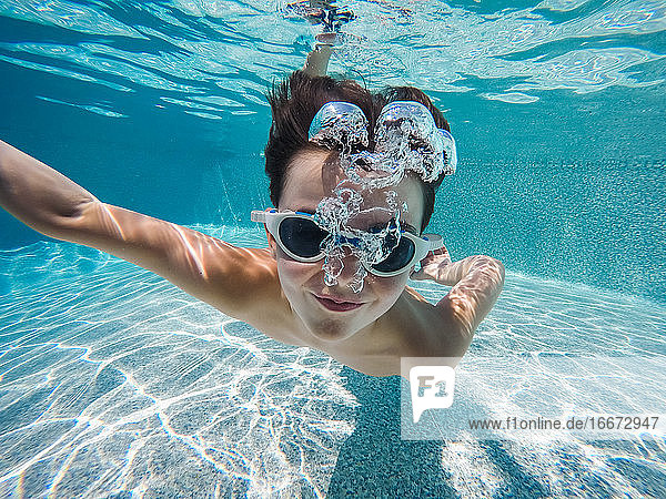 Unterwasserbild eines Jungen  der mit Schwimmbrille in einem Pool schwimmt.