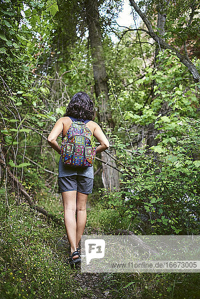 Young girl walking in the woods. She has a backpack on her back.