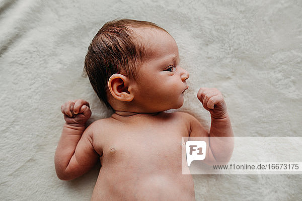 Nahaufnahme des Kopfes eines neugeborenen Babys  das zur Seite schaut  sowie Schultern und Arme