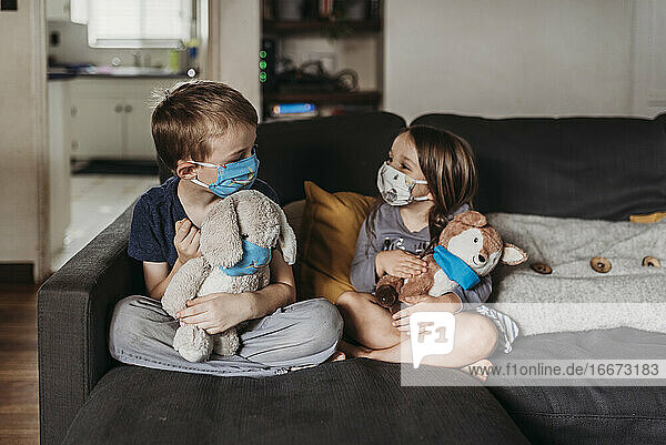 Mädchen im Vorschulalter und Junge im Schulalter mit Masken sitzen auf der Couch