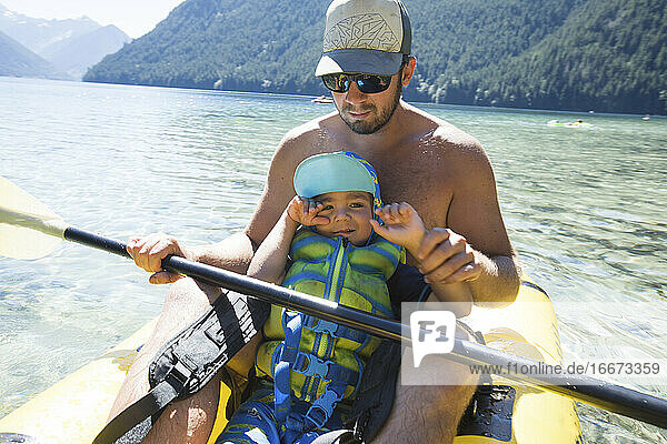 Father helping son paddle an inflatable kayak.