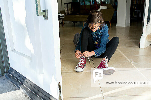 Teenager-Mädchen sitzt auf dem Kachelboden und bindet ihre brandneuen Schuhe zu