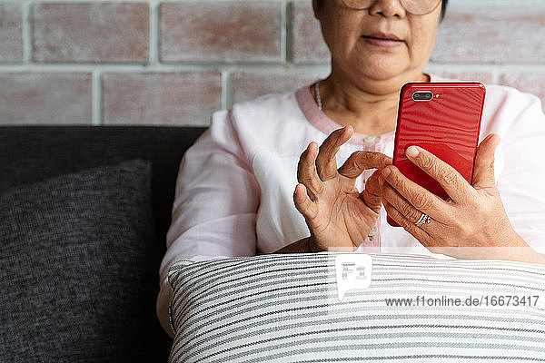 senior woman using mobile phone while sitting on sofa at home