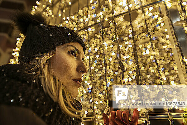 ein junges Mädchen mit einem Hut  das durch die Weihnachtsbeleuchtung schaut