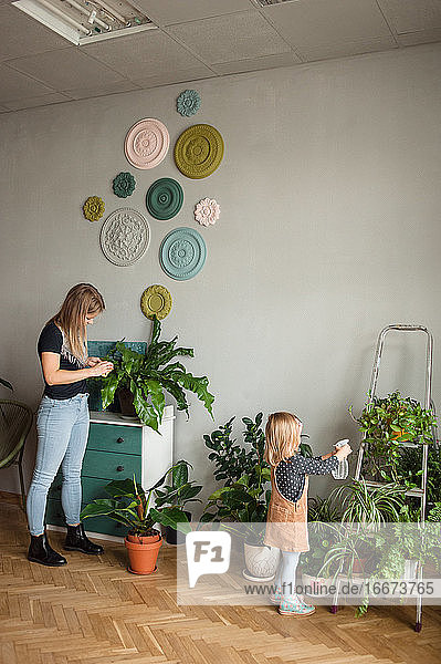 Frau und Kind kümmern sich um Grünpflanzen in einer gemütlichen modernen Wohnung.