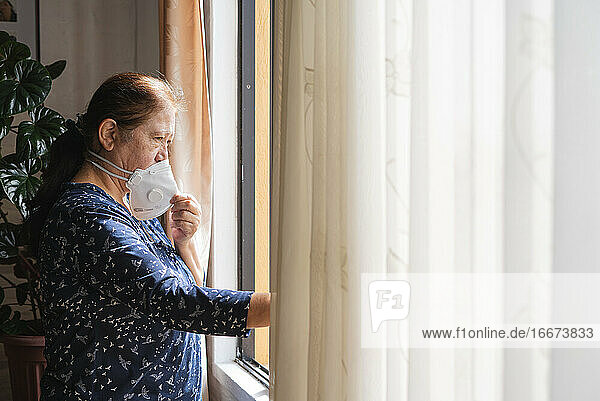 Frau im Haus während der Quarantäne mit Blick durch das Fenster nach draußen