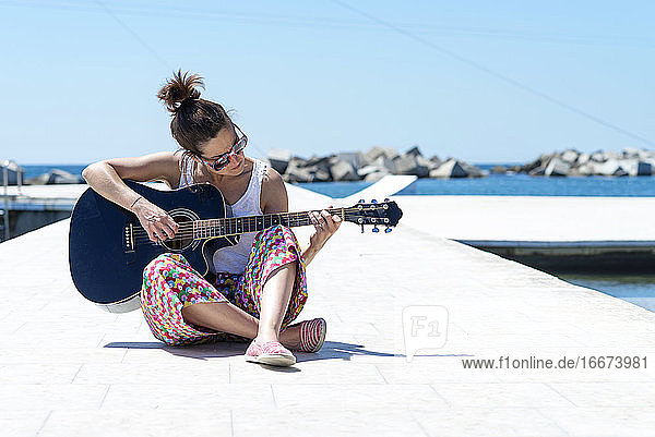 Junge Frau sitzt auf einem Boden und spielt Gitarre