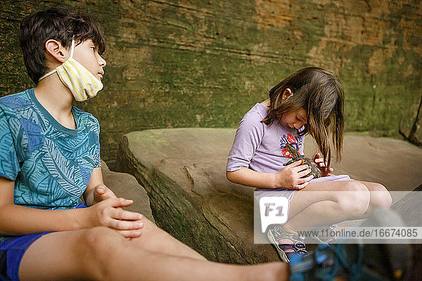 Two children sit in a rocky gorge playing with a small painted turtle