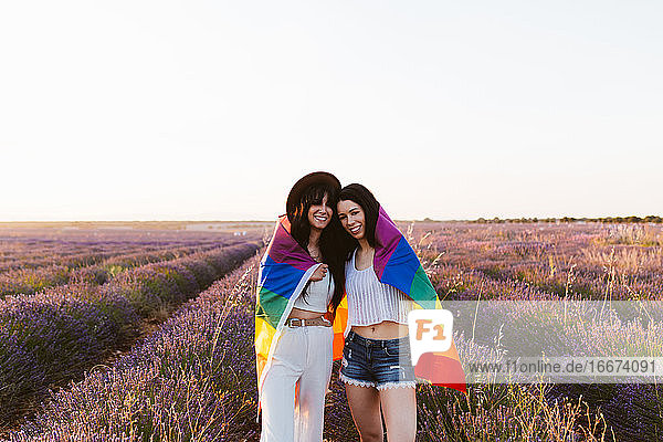 Freundinnen in einem Lavendelfeld lächelnd mit lgbt Stolz Flagge
