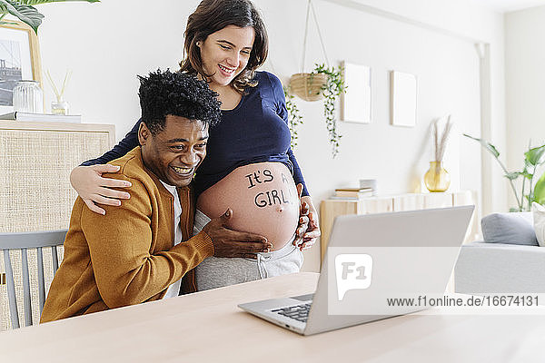 Ehemann und schwangere Frau feiern die Ergebnisse des Ultraschalls vor einem Laptop  auf dem ein Satz steht  dass es ein Mädchen ist. Konzept der Elternschaft