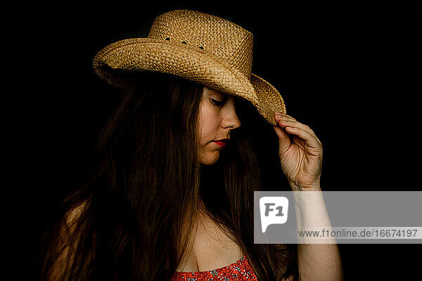 Traurige Dame mit Cowboyhut kippt ihren Hut in dramatischem Licht nach unten