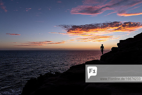 silhouette eines mannes auf einer klippe mit sonnenuntergang über dem ozean in hawaii