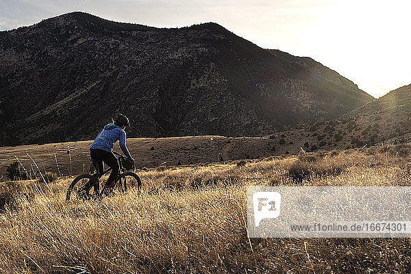 Young woman mountain biking uphill during sunset in mountains