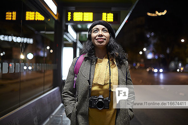 woman standing with a camera waiting at the bus station at night