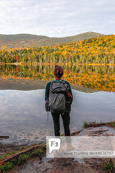 Young woman staring out at colorful trees reflecting in lake water.