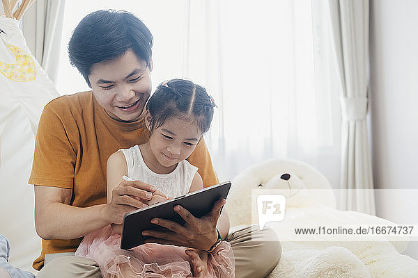 Kleines Mädchen und junger Vater genießen die gemeinsame Nutzung des Tablets.