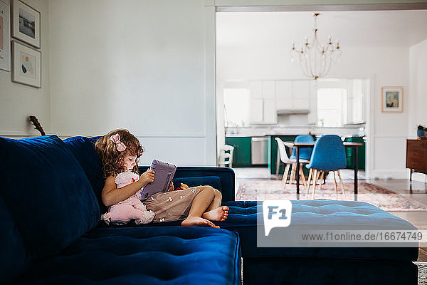 Young girl sitting on couch in modern living room learning on tablet