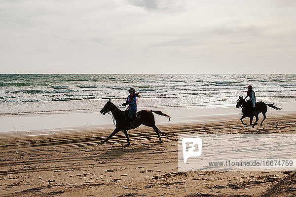 Zwei Jockeys beim Rennen mit andalusischen Pferden im Gegenlicht am Strand