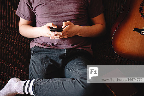 Junger Mann benutzt sein Smartphone  während er zu Hause auf dem Sofa sitzt