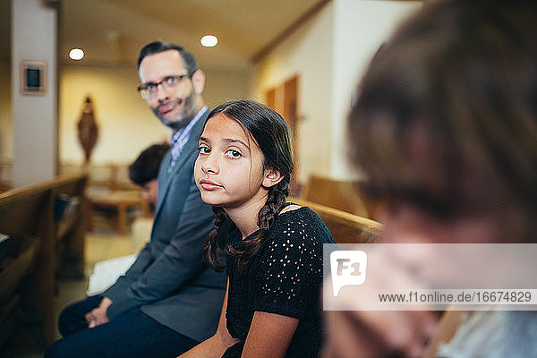 Girl in church pew with father next to her making a silly face