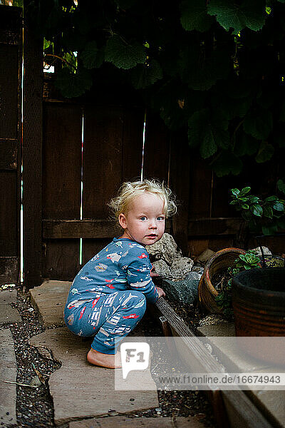 Zwei Jahre alter Junge im Schlafanzug hockt im Vorgarten unter einer Weinrebe
