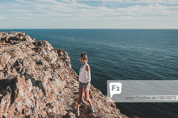 Junge Frau auf einer Klippe mit Blick auf das Meer im Sommer in Portugal