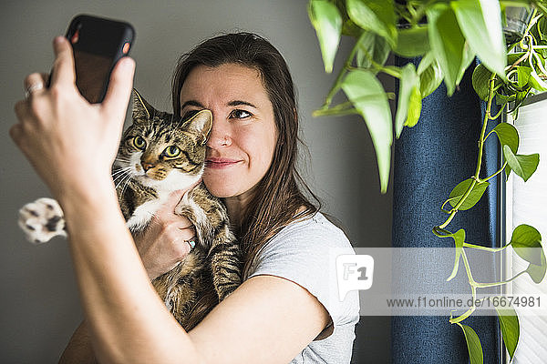 Frau zu Hause  die Selfies mit ihrer Katze am Fenster macht