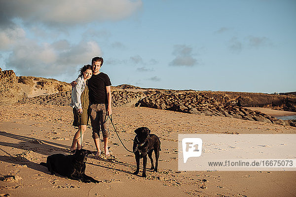 Millennial-Paar am Strand mit zwei schwarzen Labradoren
