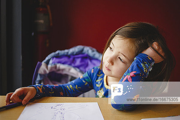 Ein kleines Mädchen mit Zeichenpapier und Stift geht verträumt zum Fenster hinaus