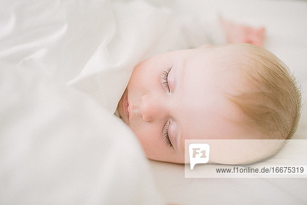 Friedlich und ätherisch schlafendes Baby umgeben von einer weißen Decke