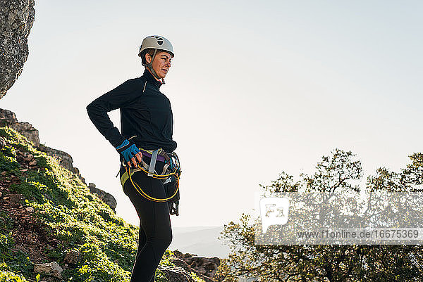 Konzept: Abenteuer. Bergsteigerin mit Helm und Klettergurt. Nachdenklich stehend auf einem Felsen auf dem Gipfel des Berges. Solare Leuchterscheinung. Via ferrata in den Bergen.