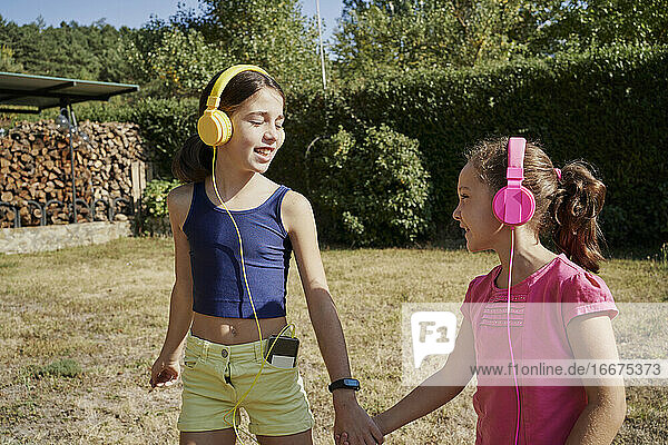 Kleine Mädchen  die sich umarmen und mit gelben und rosa Kopfhörern im Garten Musik hören. Sommer Konzept