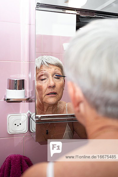 Kaukasische ältere Frau malt ihre Augen in ihrem Heimspiegel
