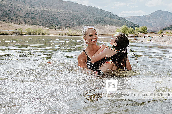 Happy mom and daughter playing together in a lake on a sunny day