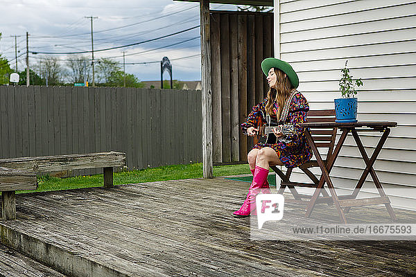 Eine stilvolle Sängerin sitzt auf einer Terrasse in einem Hinterhof und spielt Gitarre