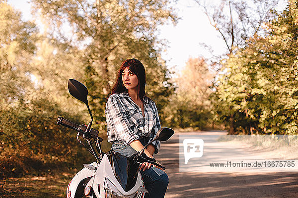 Nachdenkliche junge Frau  die auf einem Motorrad sitzend wegschaut