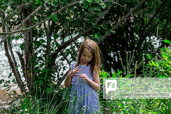 young girl surrounded by green grass playing with a flower