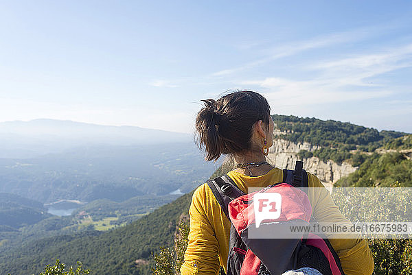 Rückansicht einer jungen Frau  die auf einem hohen Berg steht und die Aussicht betrachtet