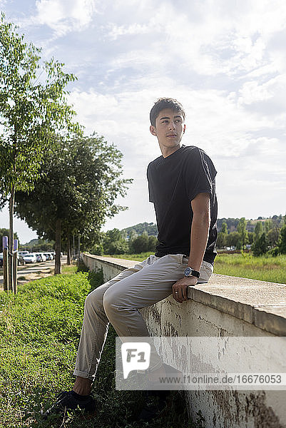 Young smiling guy sitting on fence while looking away