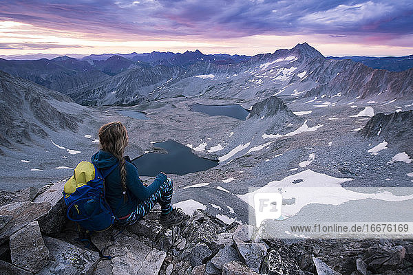 Wanderin  die bei Sonnenuntergang auf einem Felsen sitzend die Berge betrachtet