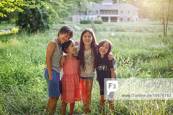 Happy children stand with arms around each other in sunlit field